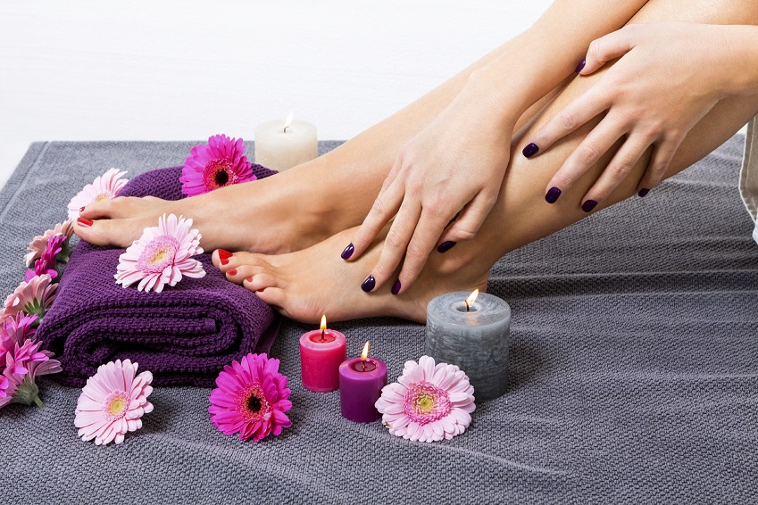 Overhead view of the bare feet of a woman with beautiful manicured red nails resting on a purple towel surrounded by fresh colourful pink gerbera daisies in a spa or beauty salon