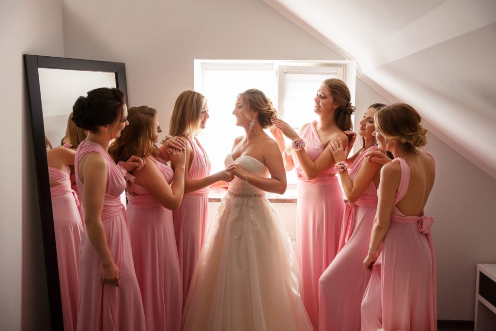 Bride with bridesmaids posing in hotel or fitting room at wedding day